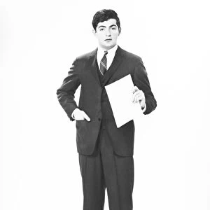 Elegant man holding blank sheet of paper in studio, (B&W), portrait