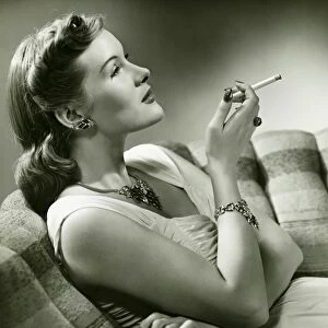 Elegant woman sitting on couch, smoking cigarette, (B&W)