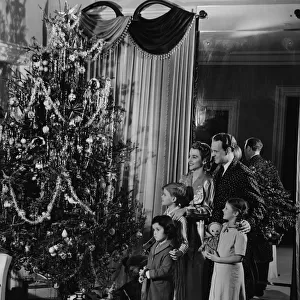 Family with three children (4-9) standing at Christmas tree, (B&W)