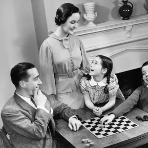 Family with two children (8-9) playing checkers (B&W), elevated view