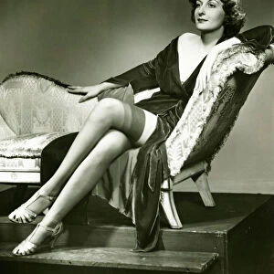 Fashionable woman in stockings sitting on chaise longue, (B&W), portrait