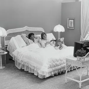 Father and mother with daughter lying on bed watching tv, smiling