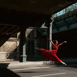 Female ballet dancer dancing with pointes in the street with a long red dress
