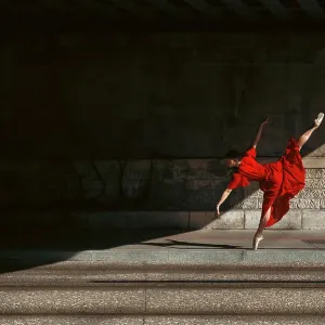 Female ballet dancer dancing with pointes in the street with a long red dress