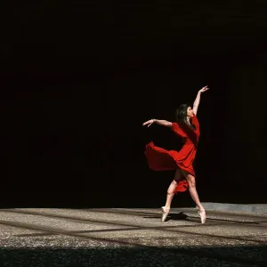 Female ballet dancer dancing with pointes in the street with a long red dress