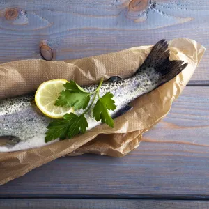 Fresh brook trout in baking paper on a wooden surface