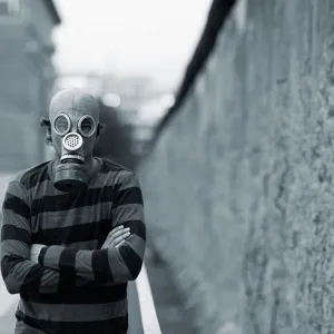 Der Gasmaskenmann steht neben der Berliner Mauer