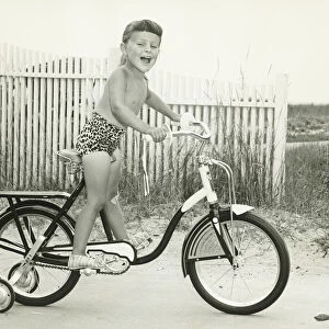 Girl (6-7) riding bicycle with side wheels, (B&W)