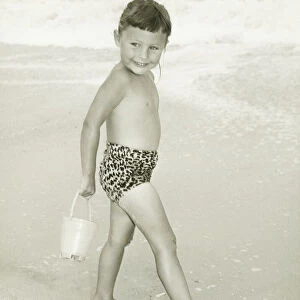 Girl (6-7) standing on beach, smiling, (B&W)