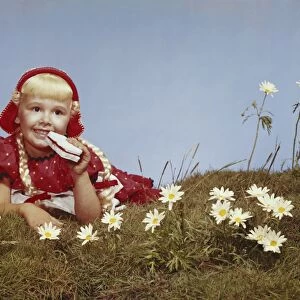 Girl lying in meadow eating bread and jam, smiling