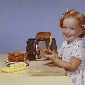 Girl spreading butter on toast, smiling, portrait
