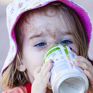 Girl, two years, face caked in sand, drinking from beverage can, Namibia
