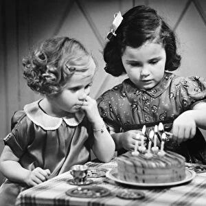 Two girls (4-5) standing at table with birthday cake (B&W)