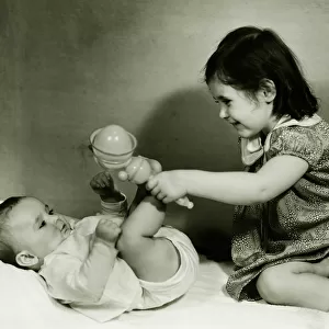 Two girls (6-12 months) (3-4) playing with rattle, (B&W)