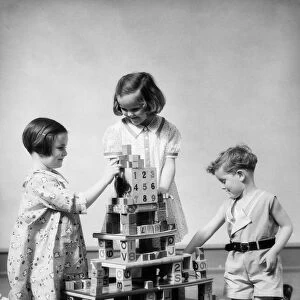 Two girls and one boy playing with alphabet building blocks constructing multi story structure