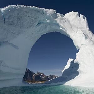 Greenland, Frederiksdal, Arched iceberg frames mountain peaks on Pamiagdluk Island