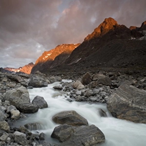 Greenland, Itilleq, setting sun lighting mountain peaks above mountain stream along Itilleq Fjord