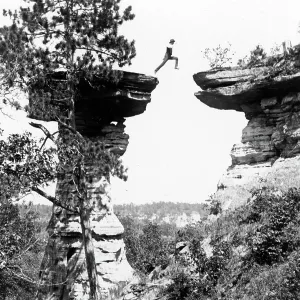 Historic photograph of man leaping between boulder in mid-air