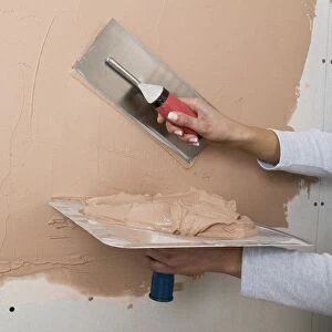 Holding a plastering hawk and spreading plaster onto a wall with a trowel