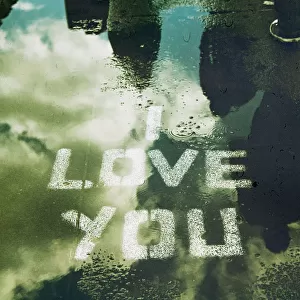 I LOVE YOU stencilled on street with rain puddle reflecting sky and passers by