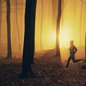 Jogger at sunrise in misty forest