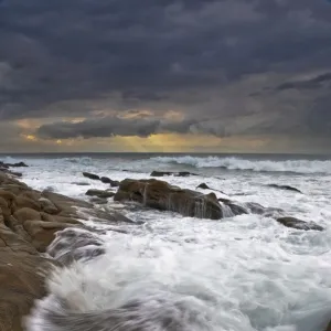 Landscape photo of ocean waves crashing onto the rocks under a stormy moody sky at sunrise. Durban, Kwazulu-Natal, South Africa