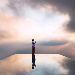 Local woman praying at sunset, reflected into water, Bali