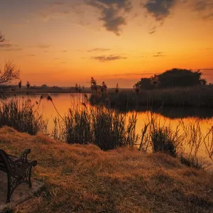 Lonesome park bench at sunset on the shores of a remote farm lake near Magaliesburg, Gauteng Province, South Africa