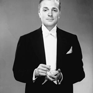 Man in dinner jacket holding cigarette and cigarette case standing in studio, (B&W), portrait