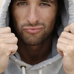Man, early 30s, wearing a hooded sweater in bad weather at the beach, portrait