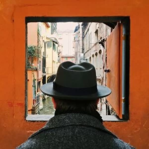 Man in hat looking at the canal through the window in Bologna, Italy