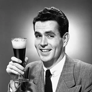 Man holding glass of beer in studio, (B&W), portrait