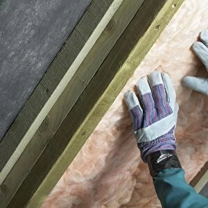 Man installing roof insulation in rafter, close-up