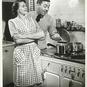 Man looking into pot in domestic kitchen, woman smiling