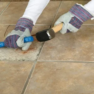 Man using club hammer and chisel to remove marble tile from floor, close-up