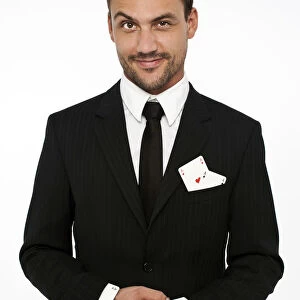 Man wearing a suit pulling an ace of diamonds out of his sleeve with other aces in his pocket