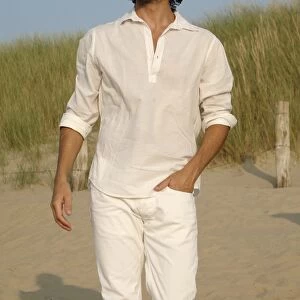 Man wearing white clothes walking in the dunes on the beach