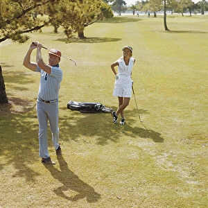 Mature couple playing golf, man swinging golf club
