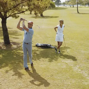 Mature couple playing golf, man swinging golf club