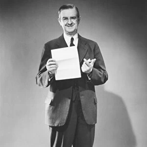 Mature man holding blank sheet of paper posing in studio (B&W), portrait