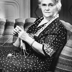 Mature woman knitting in living room (B&W), portrait