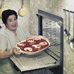 Mature woman putting food into oven, smiling, portrait
