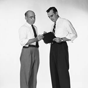 Two men standing, looking at clipboard