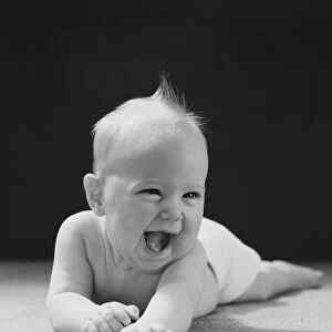 Five month old baby lying on stomach, arms outstretched, laughing