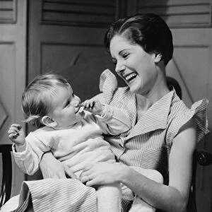 Mother laughing with child (6-12 months) on laps, (B&W)