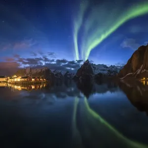 Northern lights over fishing village with mountain range on coastline at Hamnoy Northern lights over fishing village with mountain range on coastline at Hamnoy