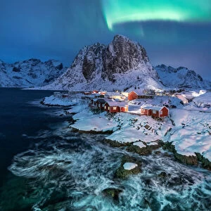 Northern lights over snowcapped mountain, village and dramatic sea in Hamnoy