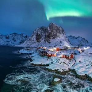 Northern lights over snowcapped mountain, village and dramatic sea in Hamnoy Northern lights over snowcapped mountain, village and dramatic sea in Hamnoy
