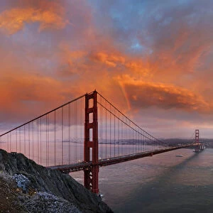 Panoramic view of the Golden Gate Bridge with a rainbow at sunset and orange-glowing storm clouds, San Francisco, California, United States