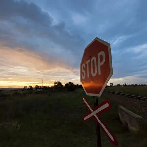 Railway crossing warning signal with Stop sign at sunset near the town of Magaliesburg, Gauteng Province, South Africa